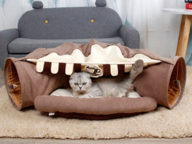 Cat lying inside a brown pet tunnel with a cozy interior, on a beige carpet.