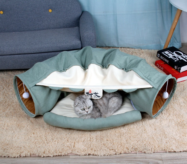 Cat lying inside a green pet tunnel on a beige carpet with a blue couch in the background.