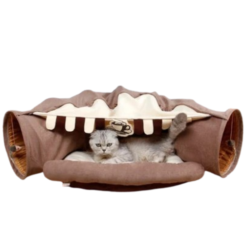 A gray cat lies inside a brown and cream cat bed designed to look like a dessert or pastry, shown against a plain white background.