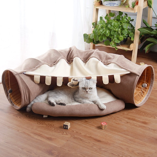 Cat lying inside a pet bed with tunnel design on a wooden floor.