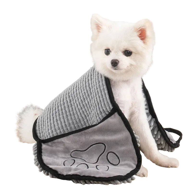 Small white dog wearing a gray knitted sweater with paw design on a wooden table.