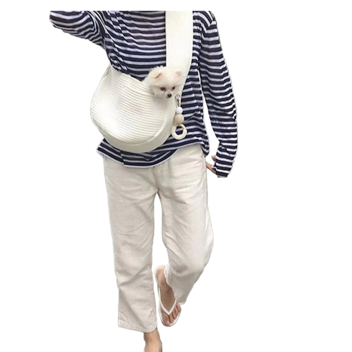 Person walking on a paved path with a small dog in a white bag slung over their shoulder.