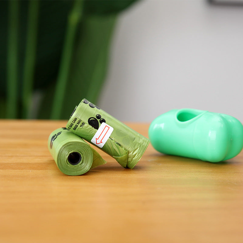Two green rolls of dog waste bags on a wooden surface with a blurred background